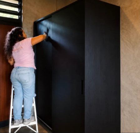 Persona ajustando un mueble alto de color negro junto a una pared con textura